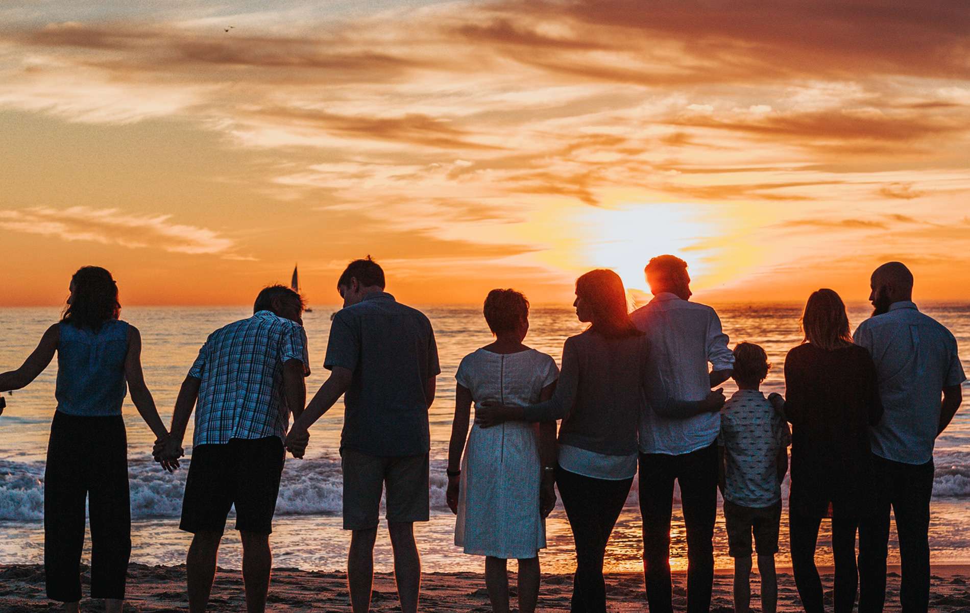 Personas de diferentes edades  mirando la puesta de sol en la playa.